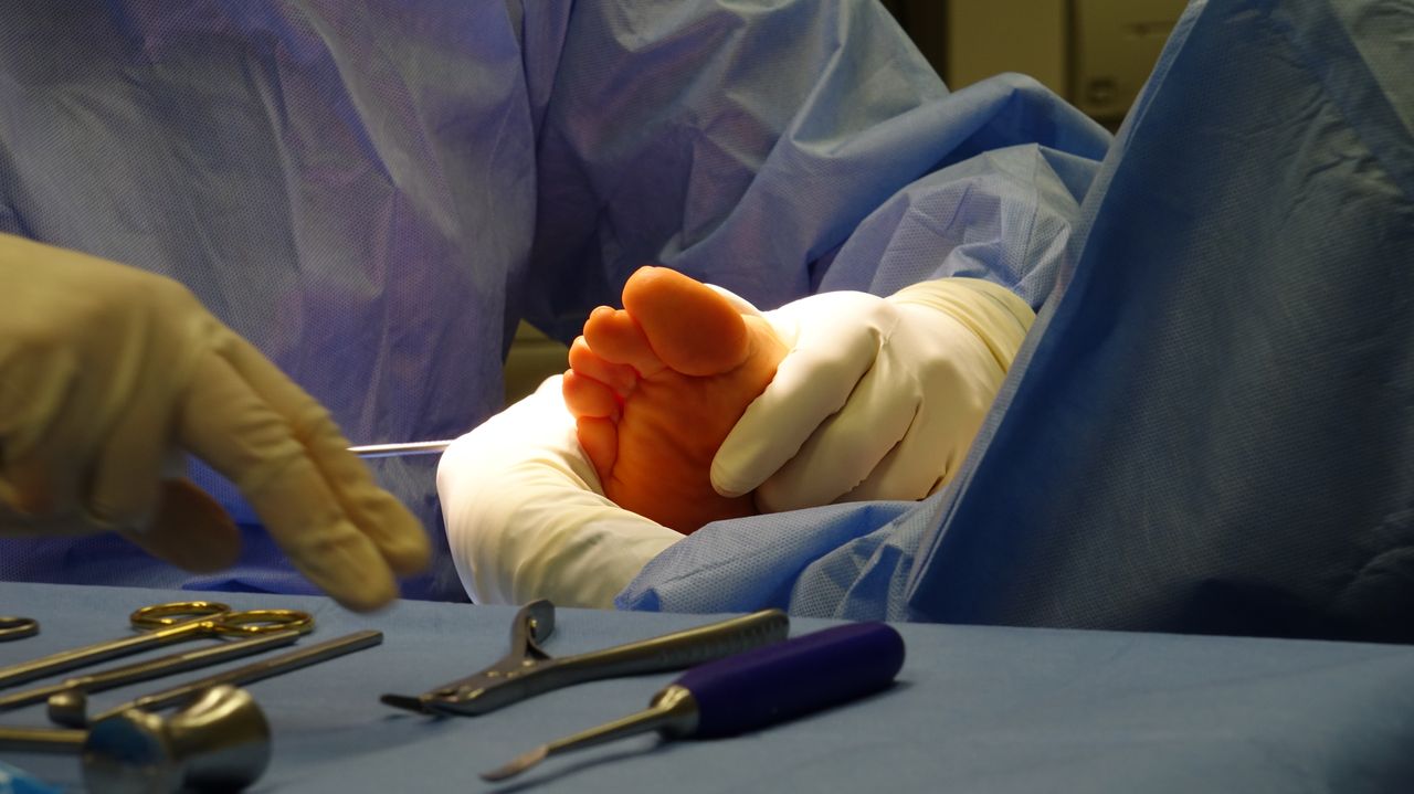 Home Gloved hands prepare for foot surgery in a sterile operating room environment.
