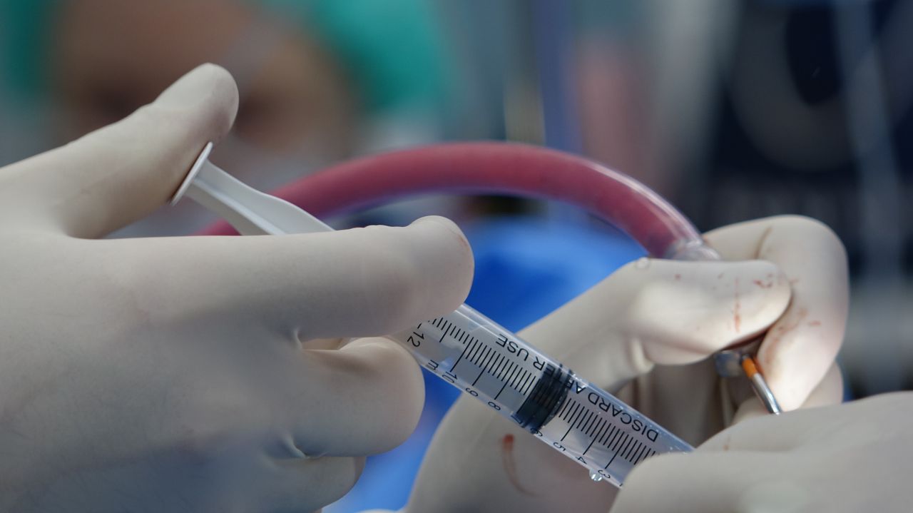 Home Surgeon's hands handling syringe during a medical procedure in a sterile operating room.