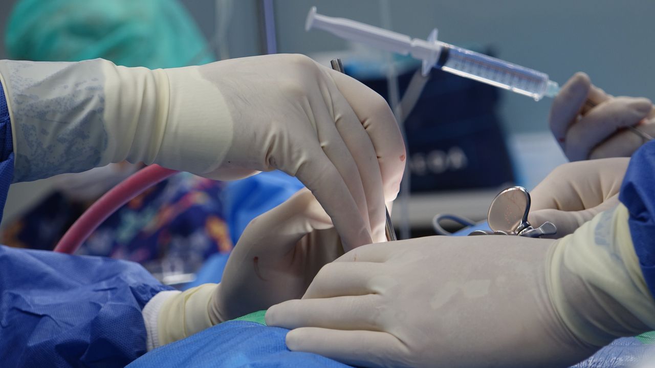 Home Close-up of surgeons' hands performing a delicate procedure with syringe and medical tools in a sterile operating room.