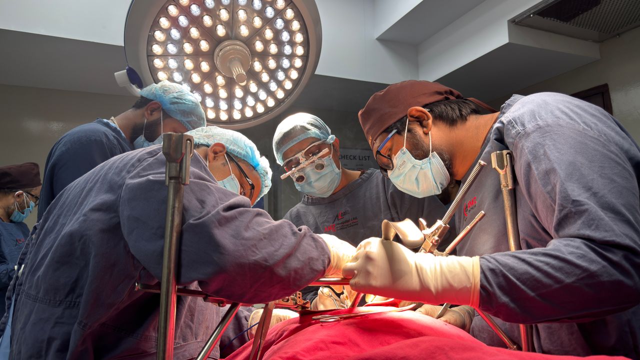 Team of surgeons focused on a surgical operation under bright lights in a hospital operating room.
